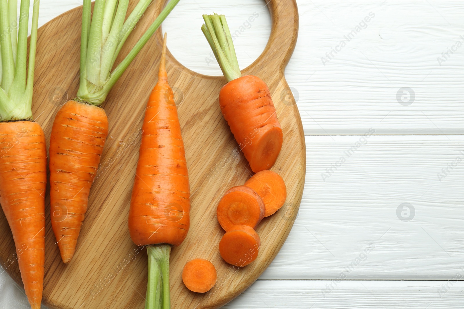 Photo of Whole and cut fresh carrots on white wooden table, top view. Space for text