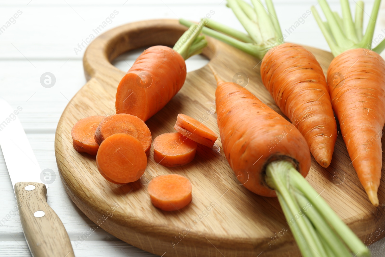 Photo of Fresh carrots and knife on white wooden table, closeup