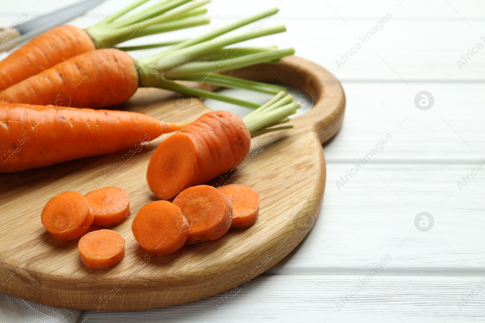 Photo of Whole and cut fresh carrots on white wooden table, closeup