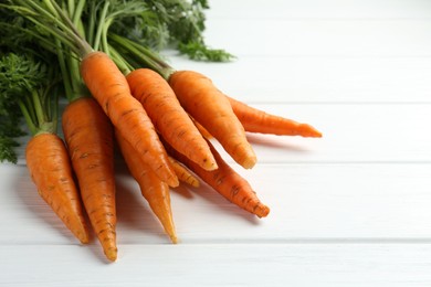 Photo of Tasty ripe juicy carrots on white wooden table, closeup. Space for text