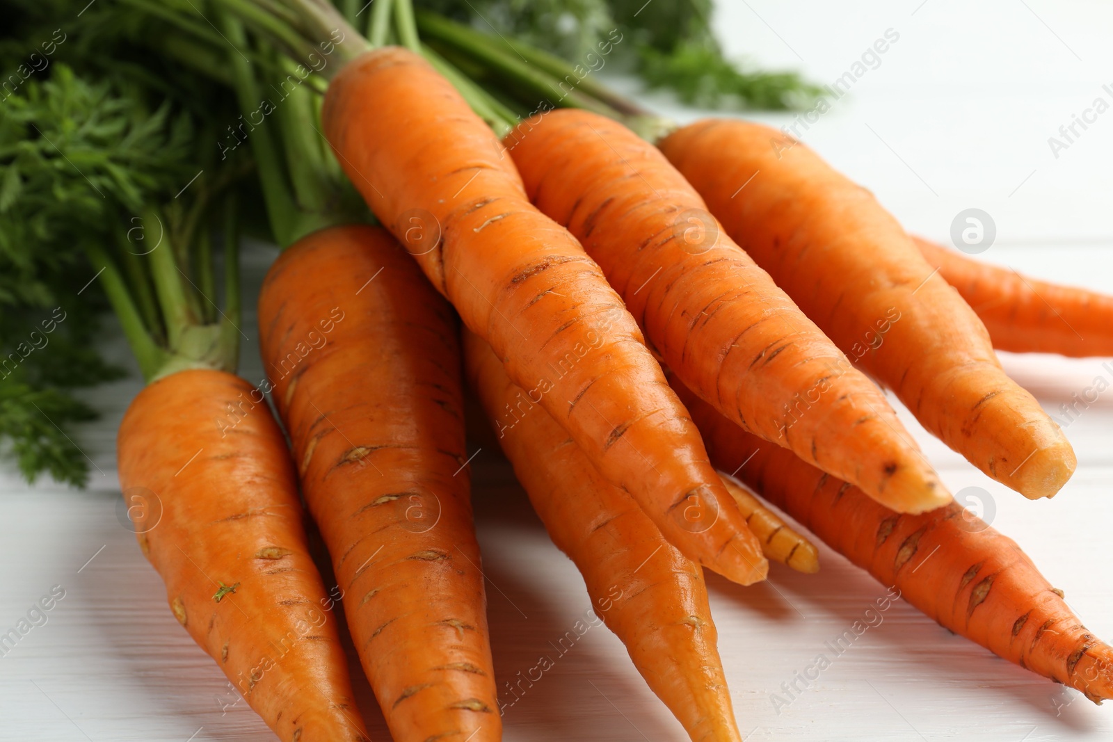 Photo of Tasty ripe juicy carrots on white wooden table, closeup