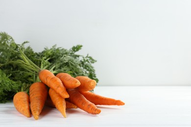 Tasty ripe juicy carrots on white wooden table, space for text