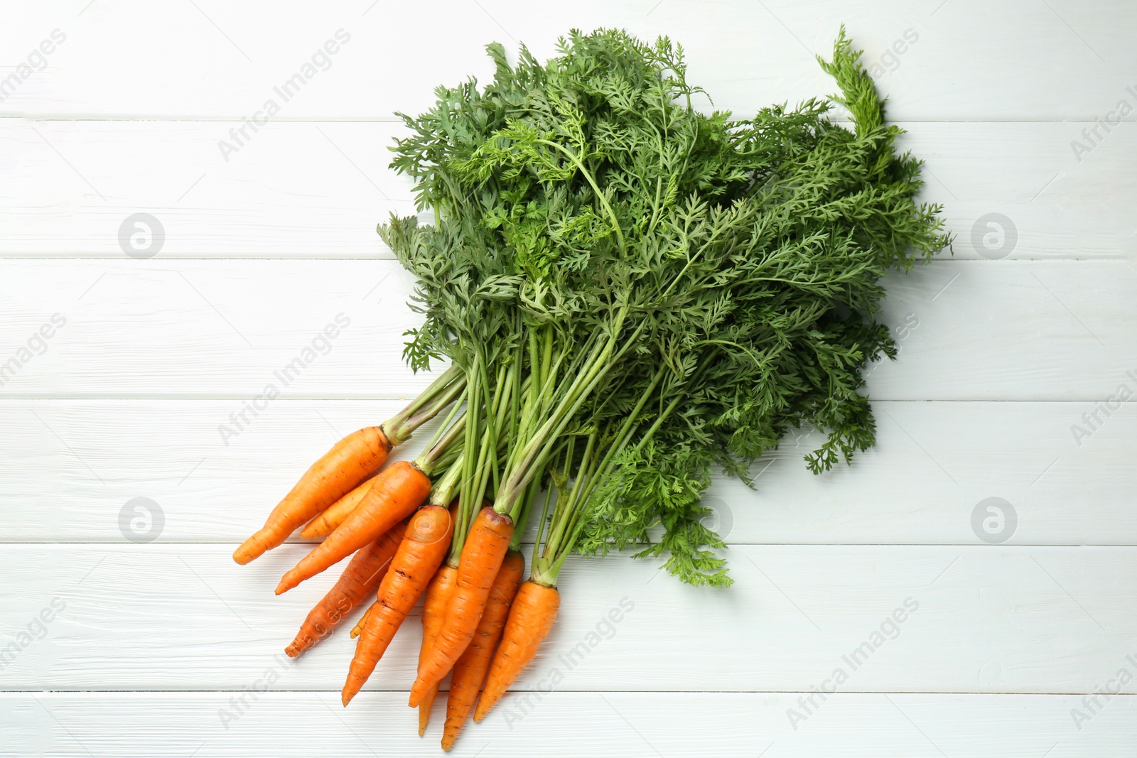 Photo of Tasty ripe juicy carrots on white wooden table, top view