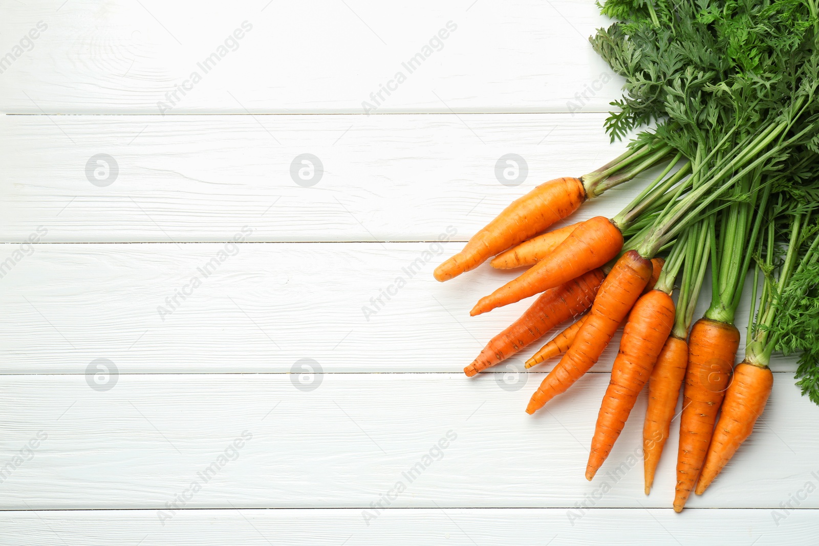 Photo of Tasty ripe juicy carrots on white wooden table, top view. Space for text