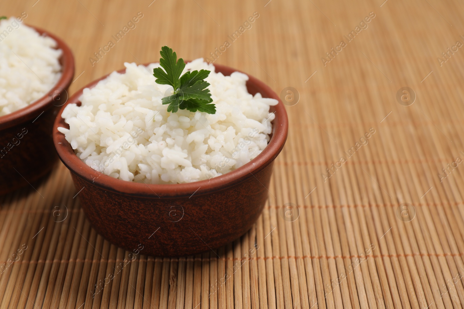 Photo of Bowls of delicious boiled rice with parsley on bamboo mat. Space for text