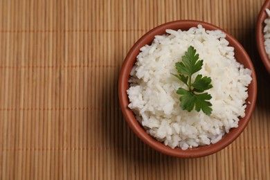 Photo of Bowls of delicious boiled rice with parsley on bamboo mat, top view. Space for text