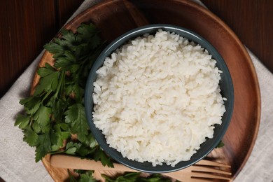 Photo of Delicious boiled rice served with parsley on wooden table, top view