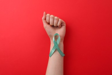 Woman holding turquoise awareness ribbon on red background, top view