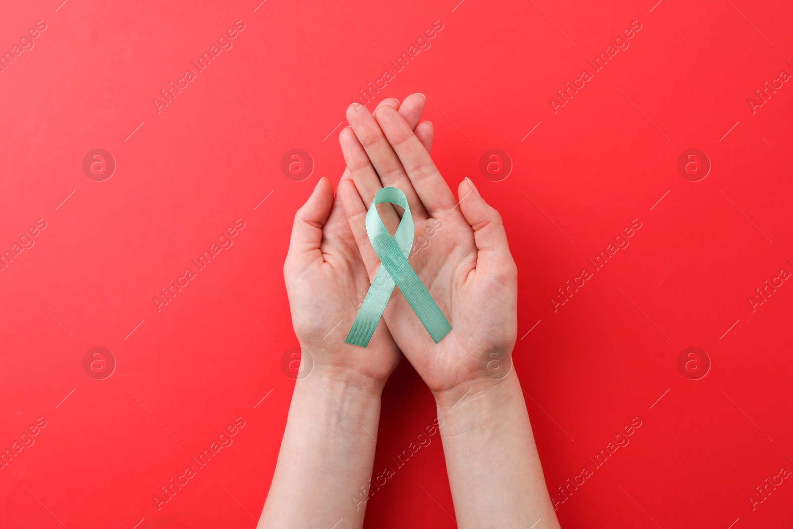 Photo of Woman holding turquoise awareness ribbon on red background, top view