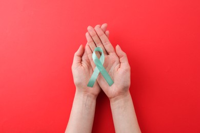 Woman holding turquoise awareness ribbon on red background, top view