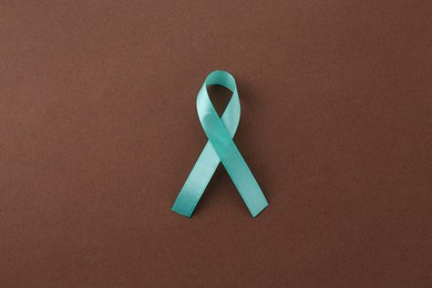 Turquoise awareness ribbon on brown background, top view