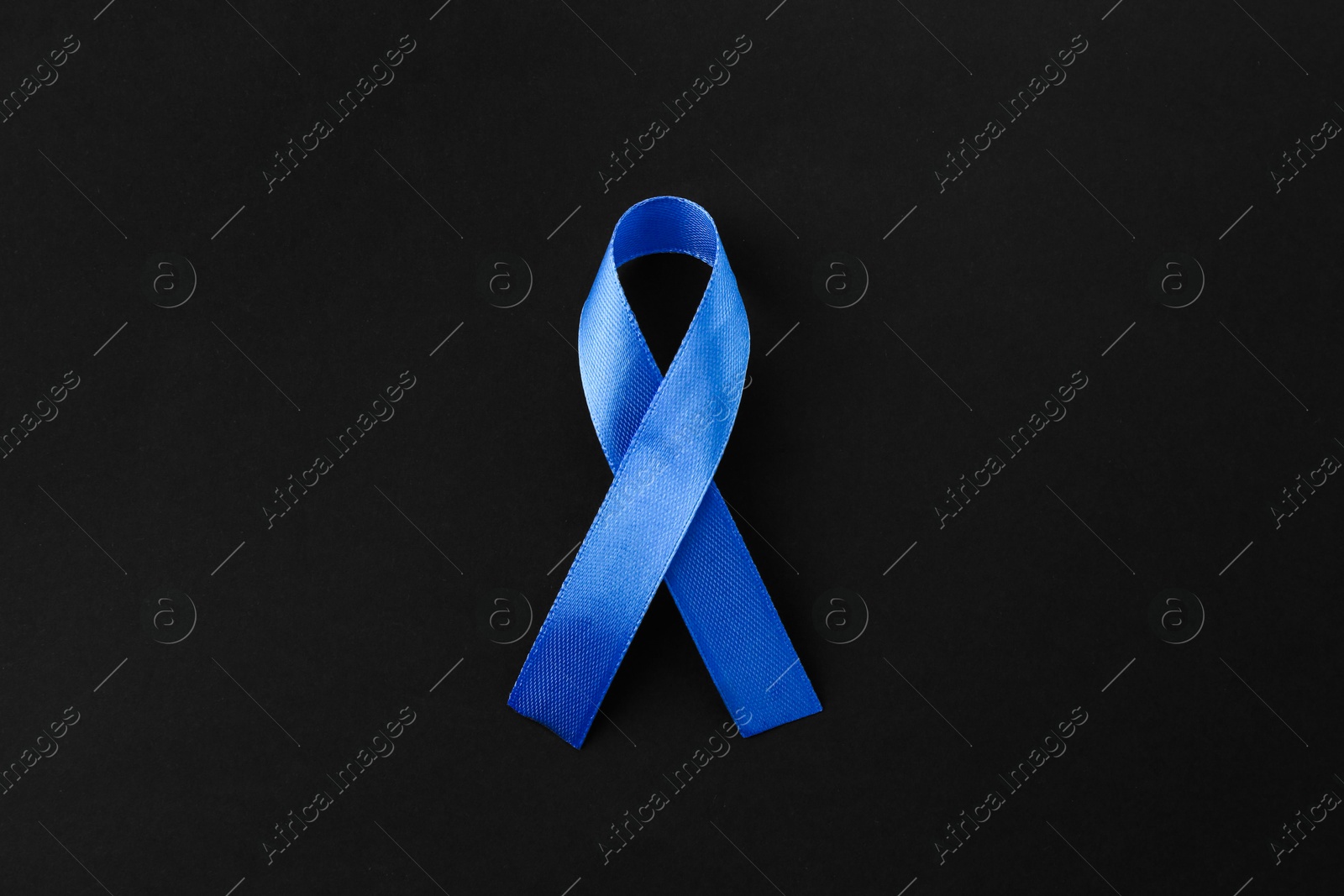 Photo of Blue awareness ribbon on black background, top view