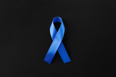 Photo of Blue awareness ribbon on black background, top view