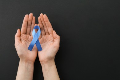 Woman with blue awareness ribbon on black background, top view. Space for text