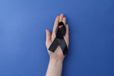 Photo of Woman with black awareness ribbon on blue background, top view