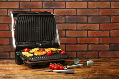 Electric grill with tasty meat, rosemary and vegetables on wooden table