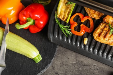 Photo of Electric grill with tasty meat, spices and vegetables on grey textured table