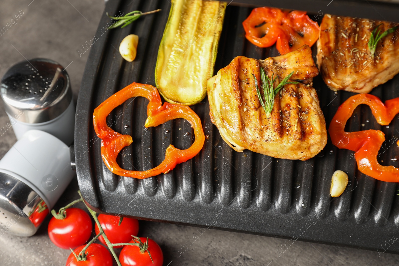 Photo of Electric grill with tasty meat, spices and vegetables on grey table