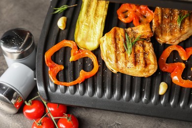 Electric grill with tasty meat, spices and vegetables on grey table