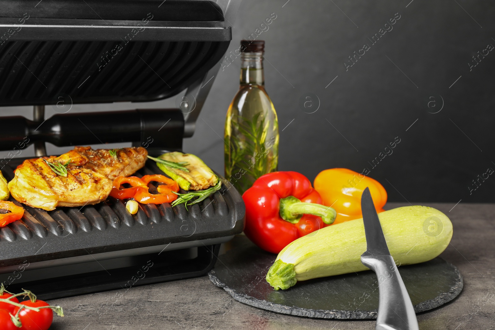 Photo of Electric grill with different products and knife on grey textured table