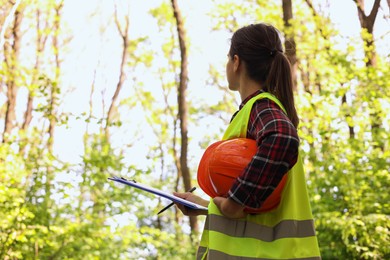 Photo of Forester with hard hat and clipboard examining plants in forest