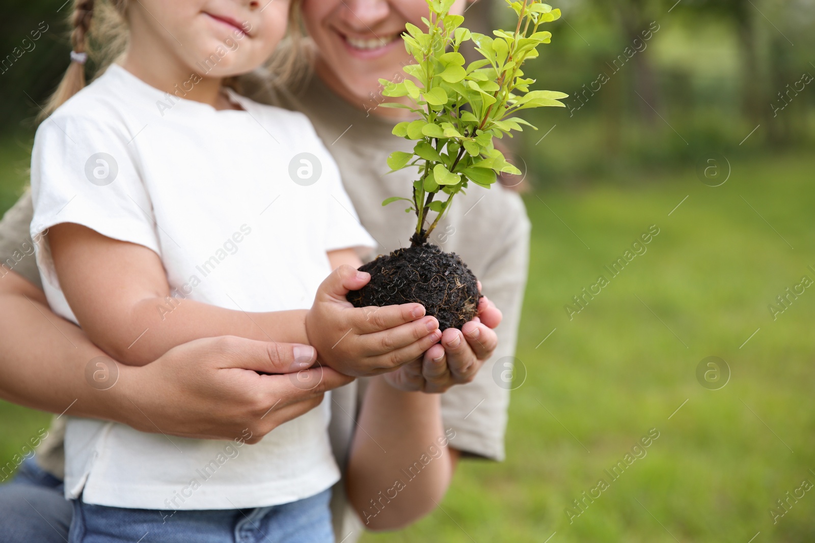 Photo of Mother and her daughter planting tree together in garden, closeup. Space for text