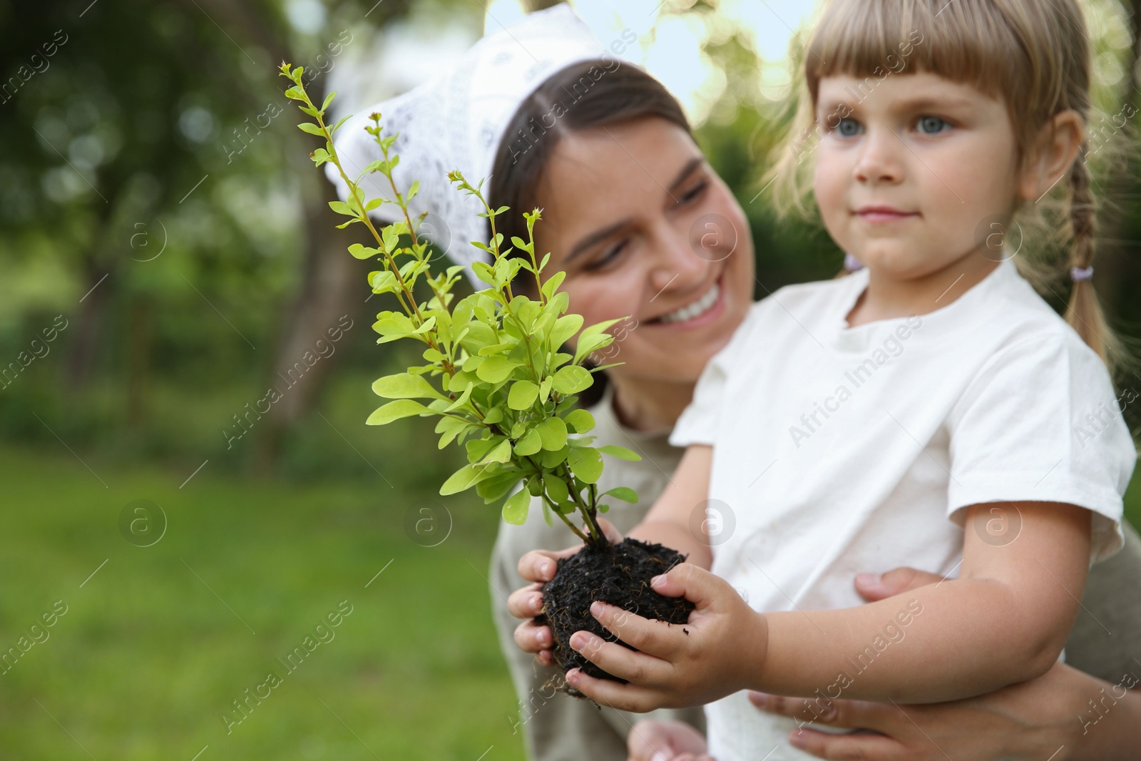 Photo of Mother and her daughter planting tree together in garden, space for text