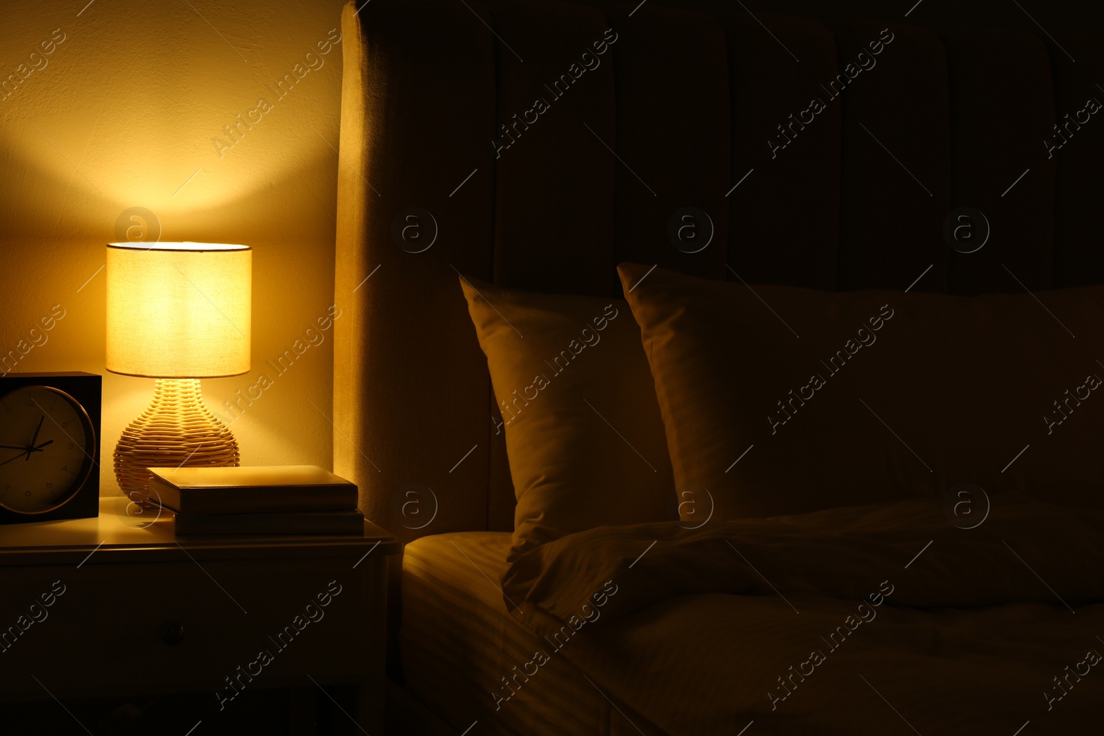 Photo of Nightlight, clock and books on bedside table near bed indoors