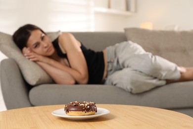 Photo of Eating disorder. Woman lying on sofa indoors, focus on donut