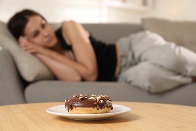 Eating disorder. Woman lying on sofa indoors, focus on donut