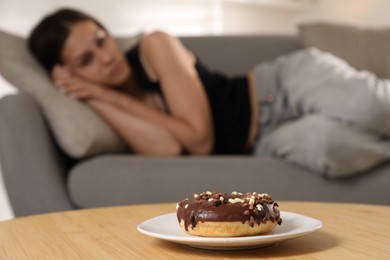Photo of Eating disorder. Woman lying on sofa indoors, focus on donut