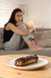 Photo of Eating disorder. Woman sitting on sofa indoors, focus on eclair