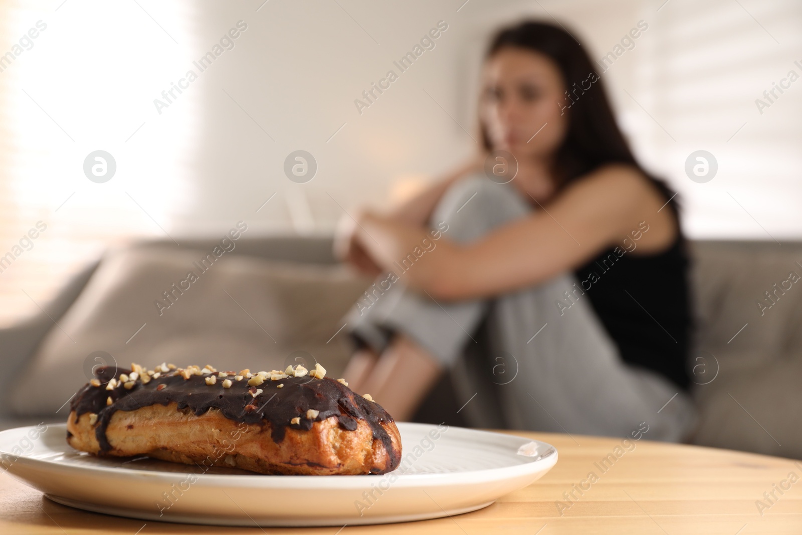 Photo of Eating disorder. Woman sitting on sofa indoors, focus on eclair