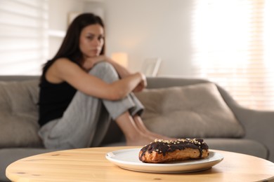 Photo of Eating disorder. Woman sitting on sofa indoors, focus on eclair