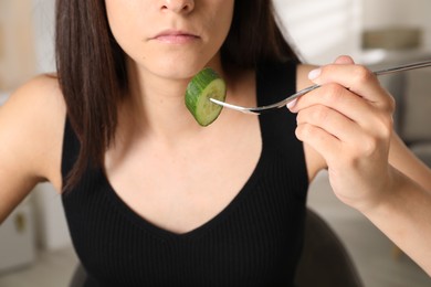 Photo of Eating disorder. Woman holding fork with cucumber indoors, closeup