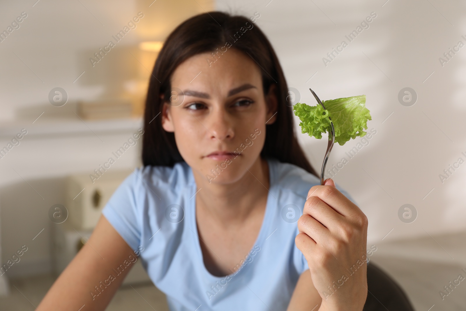 Photo of Eating disorder. Sad woman holding fork with lettuce indoors