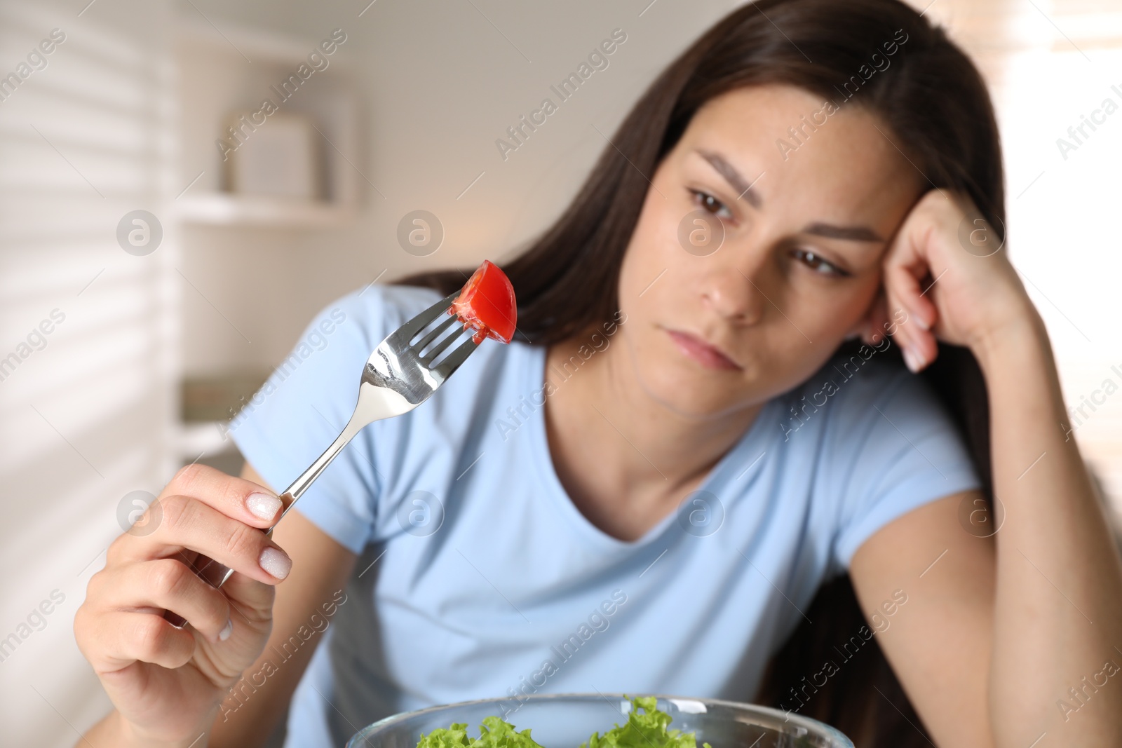 Photo of Eating disorder. Sad woman holding fork with tomato indoors