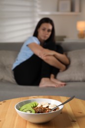 Photo of Eating disorder. Sad woman sitting on sofa indoors, focus on granola, kiwi and banana