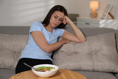 Eating disorder. Sad woman near table with meal indoors