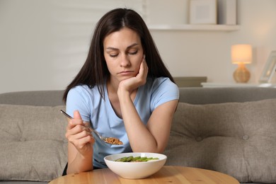 Photo of Eating disorder. Sad woman holding spoon with granola over bowl indoors
