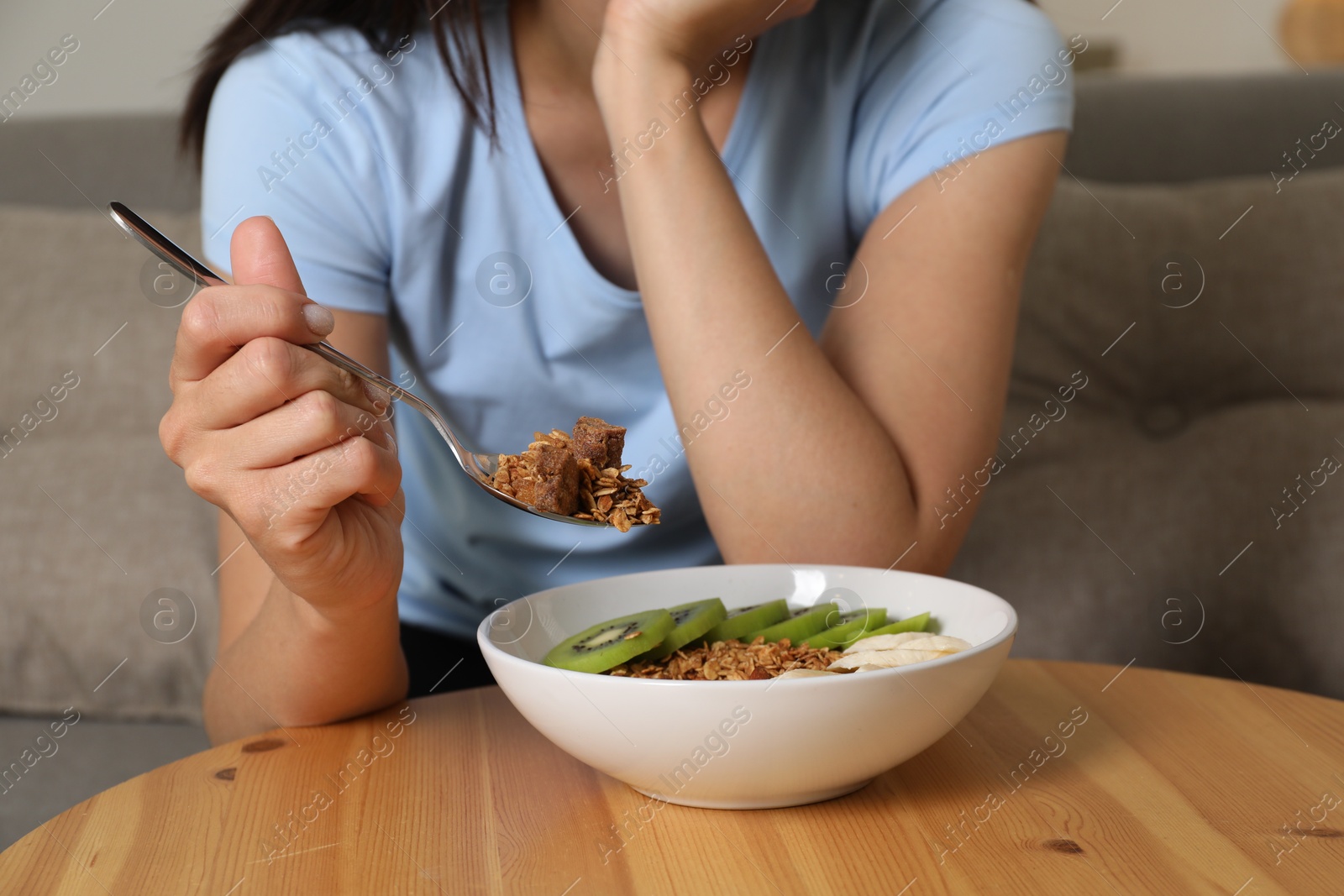 Photo of Eating disorder. Woman holding spoon with granola over bowl at table indoors, closeup