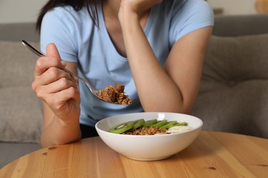 Eating disorder. Woman holding spoon with granola over bowl at table indoors, closeup