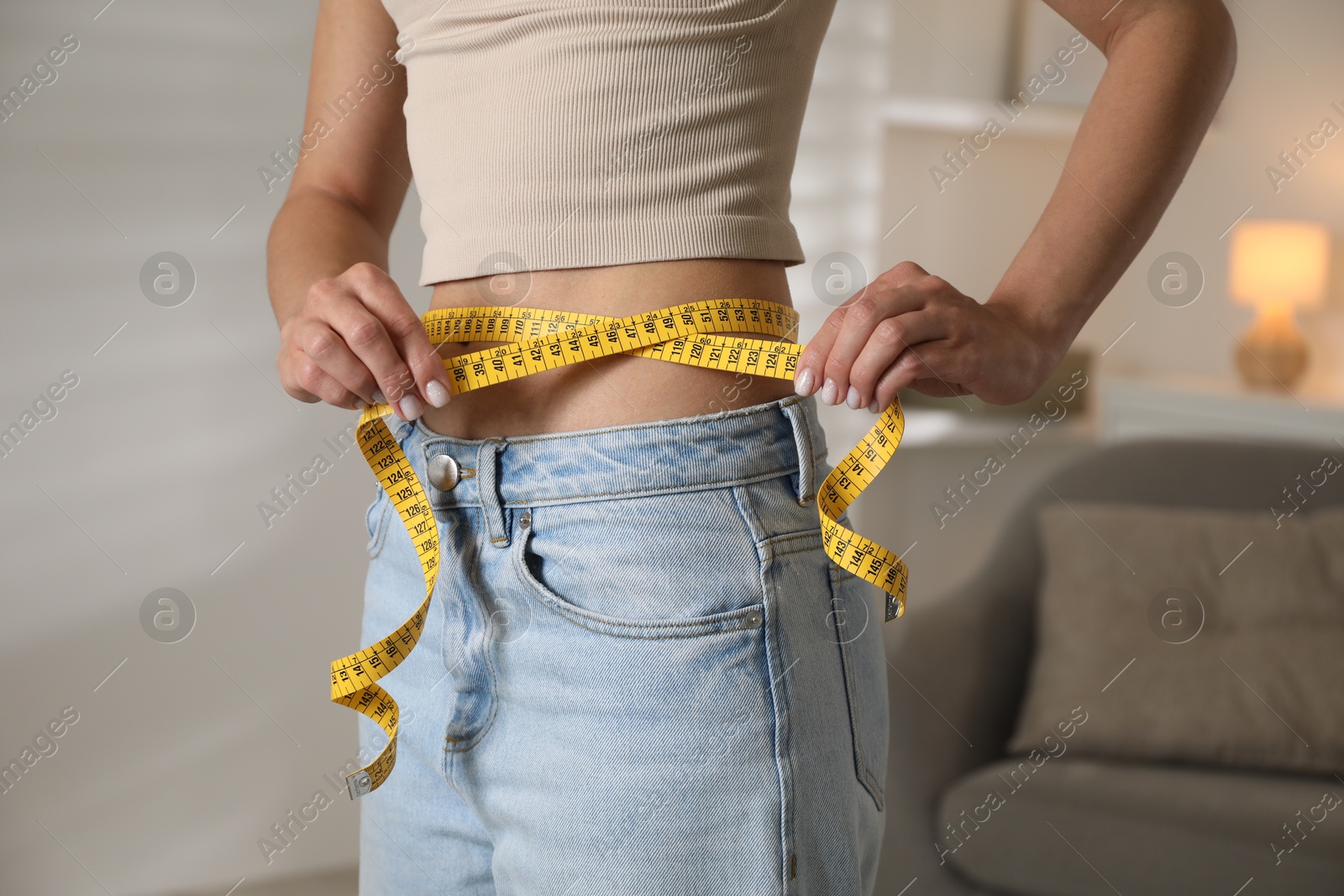 Photo of Eating disorder. Woman measuring her waist indoors, closeup