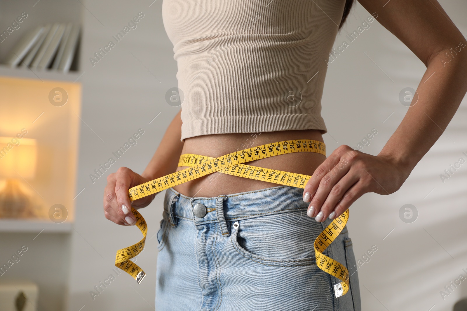 Photo of Eating disorder. Woman measuring her waist indoors, closeup