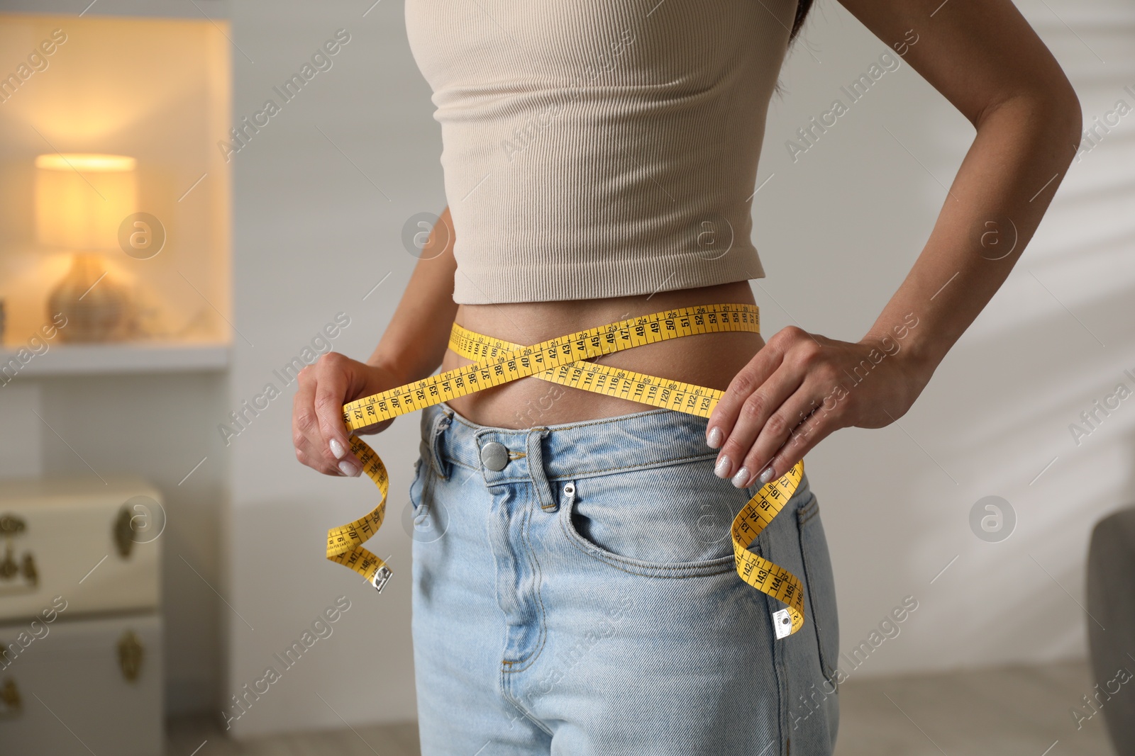 Photo of Eating disorder. Woman measuring her waist indoors, closeup