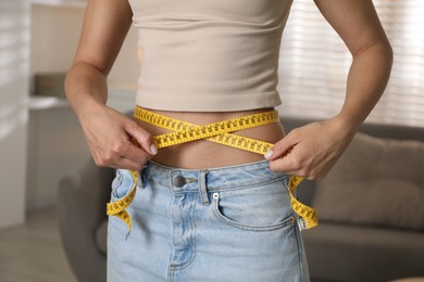 Photo of Eating disorder. Woman measuring her waist indoors, closeup