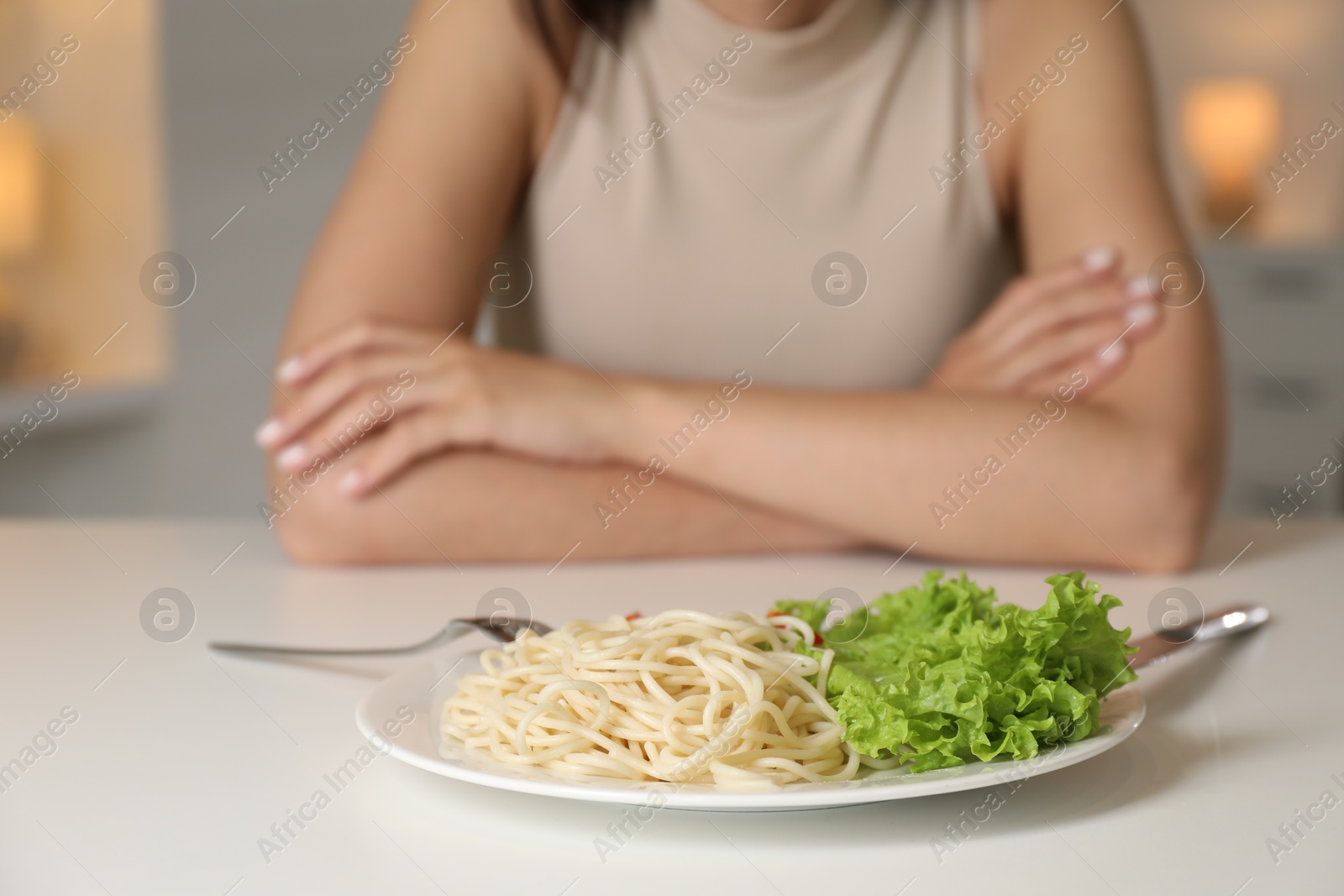 Photo of Eating disorder. Woman at white table with spaghetti and cutlery, selective focus