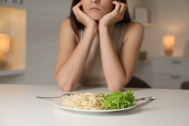 Photo of Eating disorder. Woman at white table with spaghetti and cutlery, selective focus