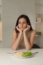 Photo of Eating disorder. Sad woman at white table with spaghetti and cutlery indoors