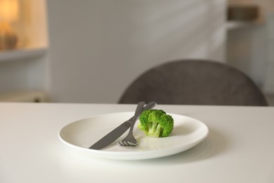 Eating disorder. Plate with broccoli and cutlery on white table indoors